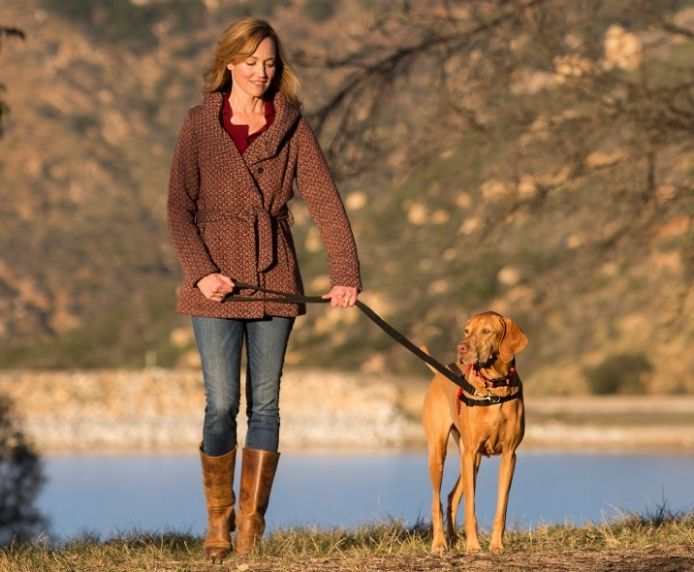 Woman walking dog wearing HALTI Front Control Harness outdoors near water and hills
