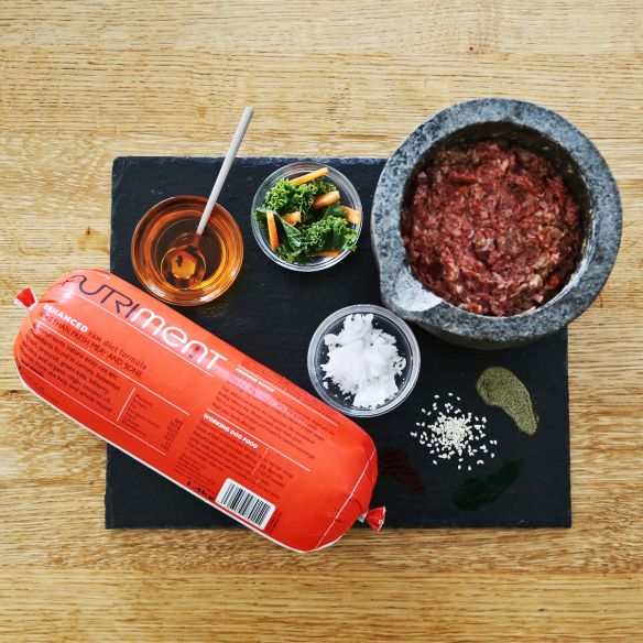 Nutriment Raw Duck Formula Dog Food with ingredients including duck meat, vegetables, and oils on a wooden table.
